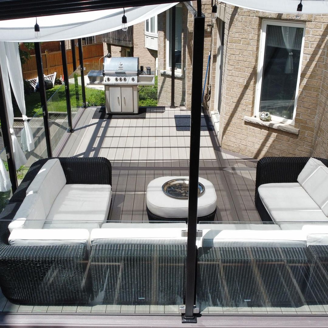 Modern outdoor patio with black wicker sofas, white cushions, a central ottoman, and a stainless steel grill.