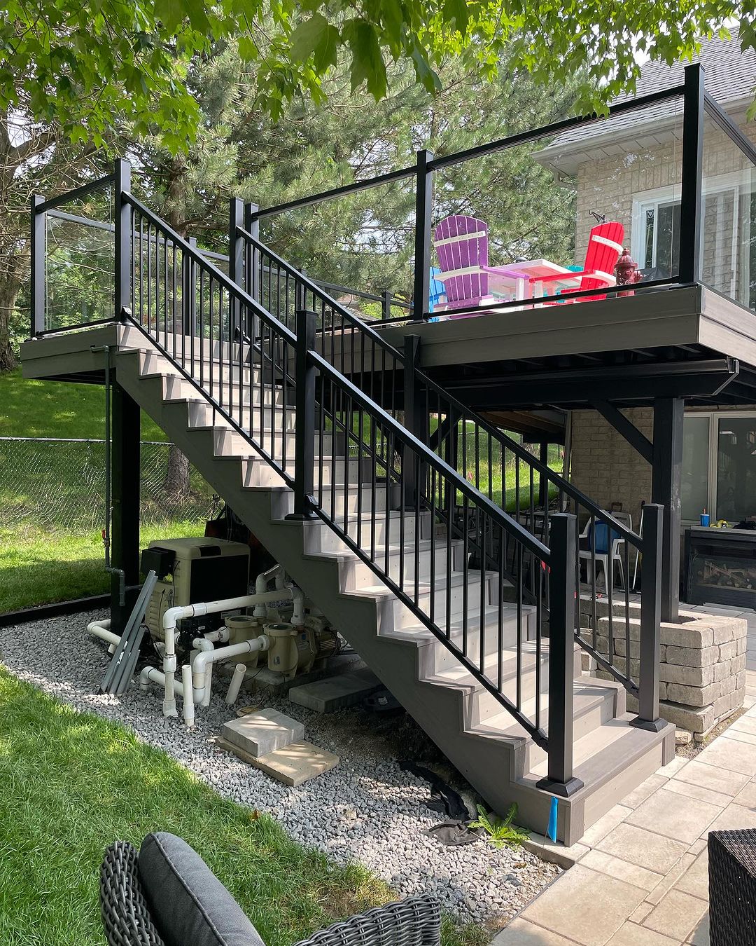 Outdoor staircase with black metal railing leading to a raised deck with colorful Adirondack chairs.