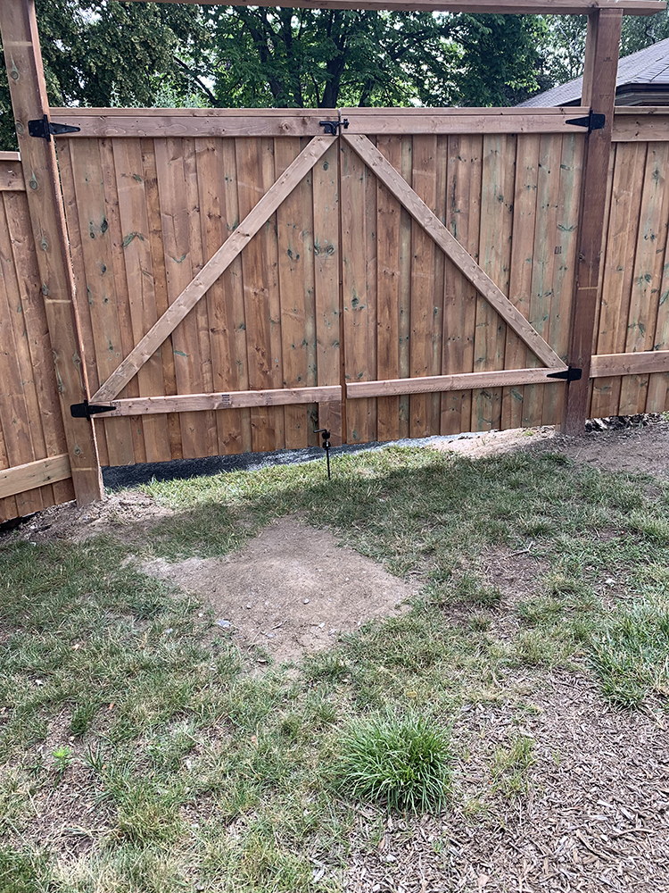 Closed wooden fence gate with diagonal support beams and patchy grass in front.
