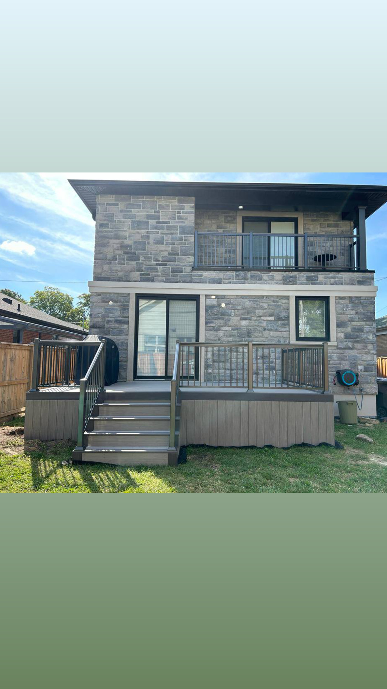 Back of a two-story stone house with a small raised deck, stairs, and a sliding glass door.