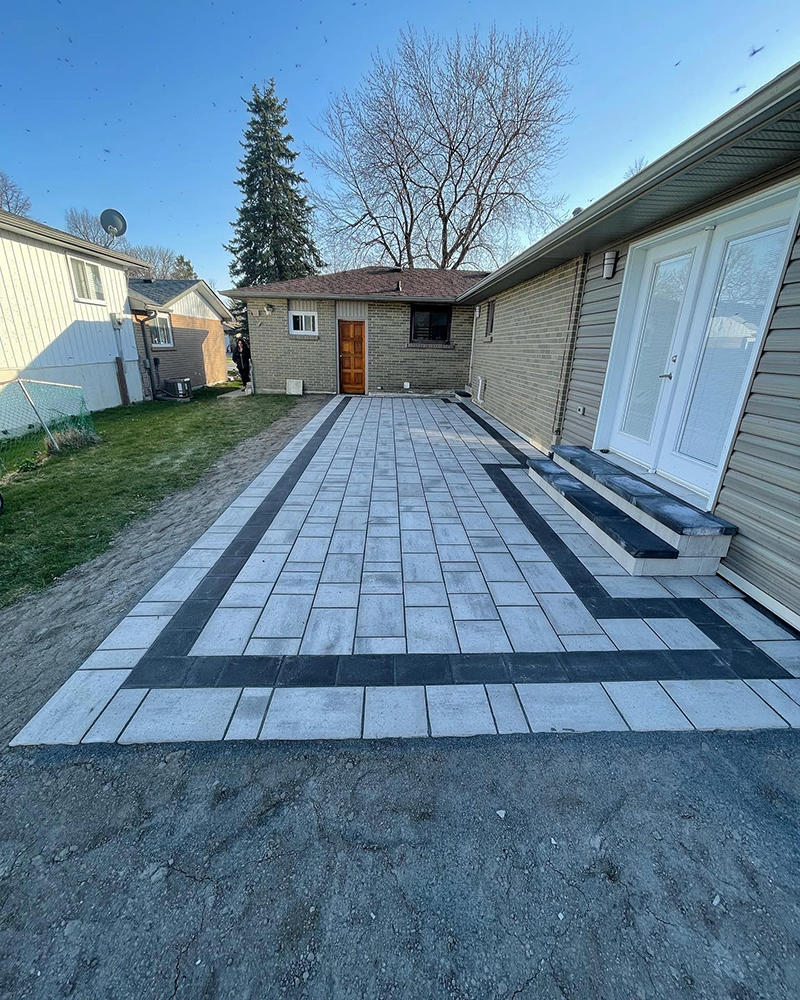 Newly installed rectangular patio with light and dark gray tiles adjacent to a house and yard.
