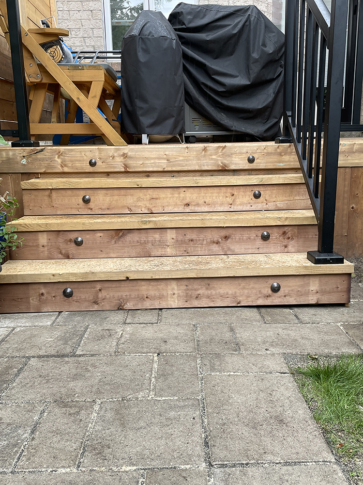 Wooden outdoor stairs with black round lights on each step and a black metal railing on the right side.