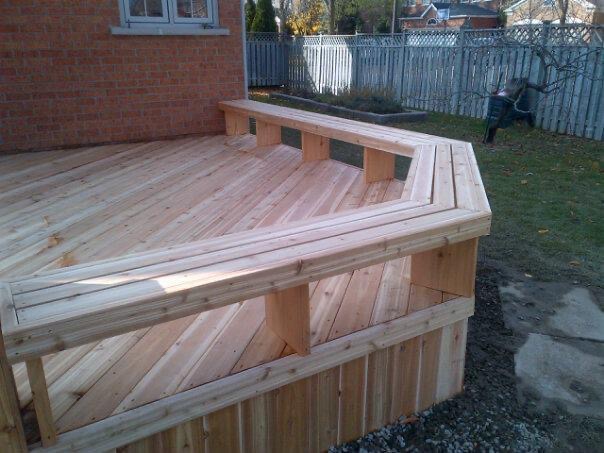 Newly built wooden deck attached to a brick house with a railing and benches.