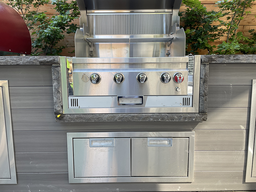 Outdoor stainless steel gas grill with open lid built into a gray countertop and cabinetry.