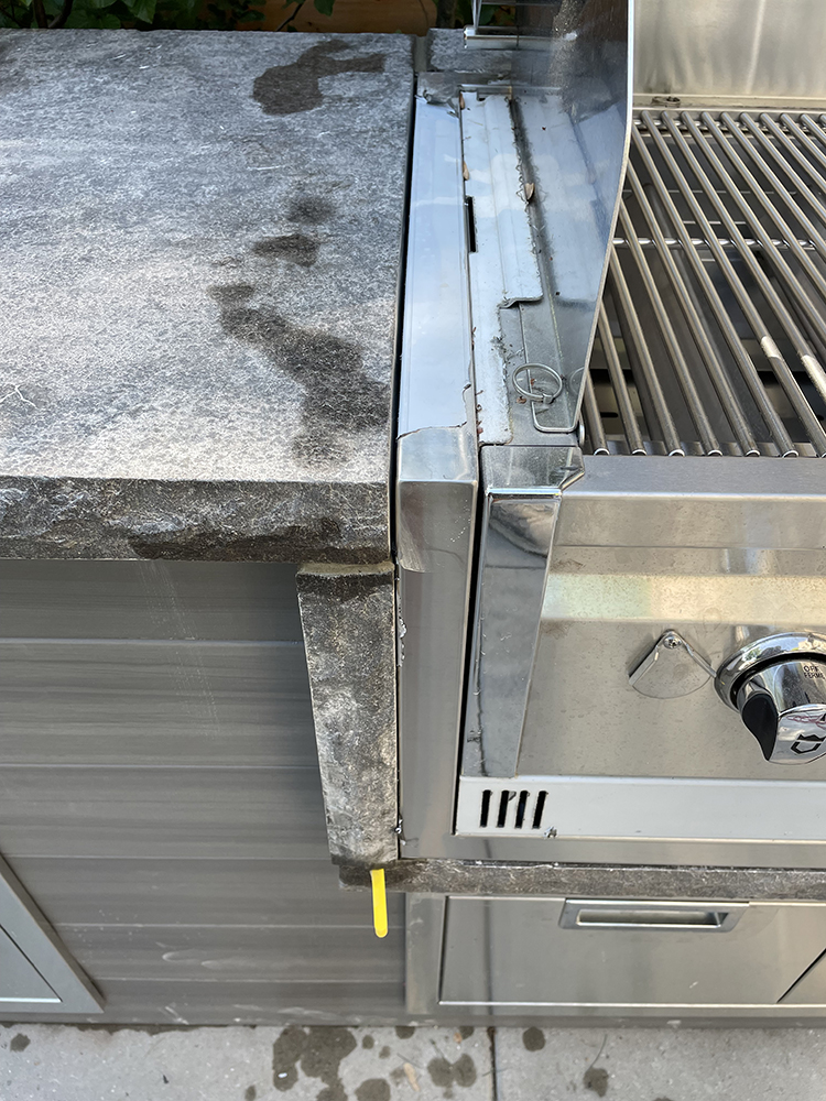 Outdoor stainless steel grill embedded in stone countertop with water stains on the surface.