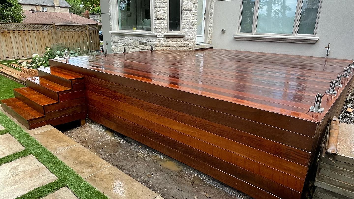 Newly constructed shiny wooden deck attached to house with stairs leading to garden.