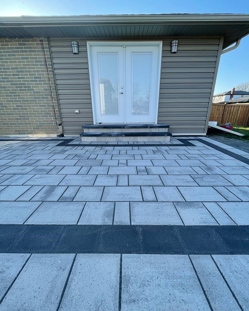 Backyard patio with light gray and dark gray rectangular pavers in front of white double French doors.