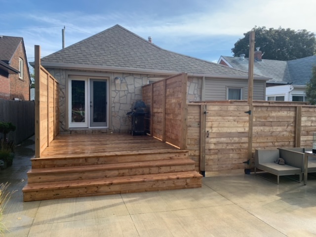 Wooden backyard deck with steps, partial privacy fence, and a barbecue grill near a house's back door.