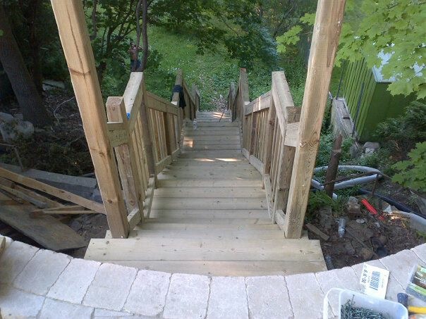 Wooden outdoor staircase with handrails descending into a green garden area.