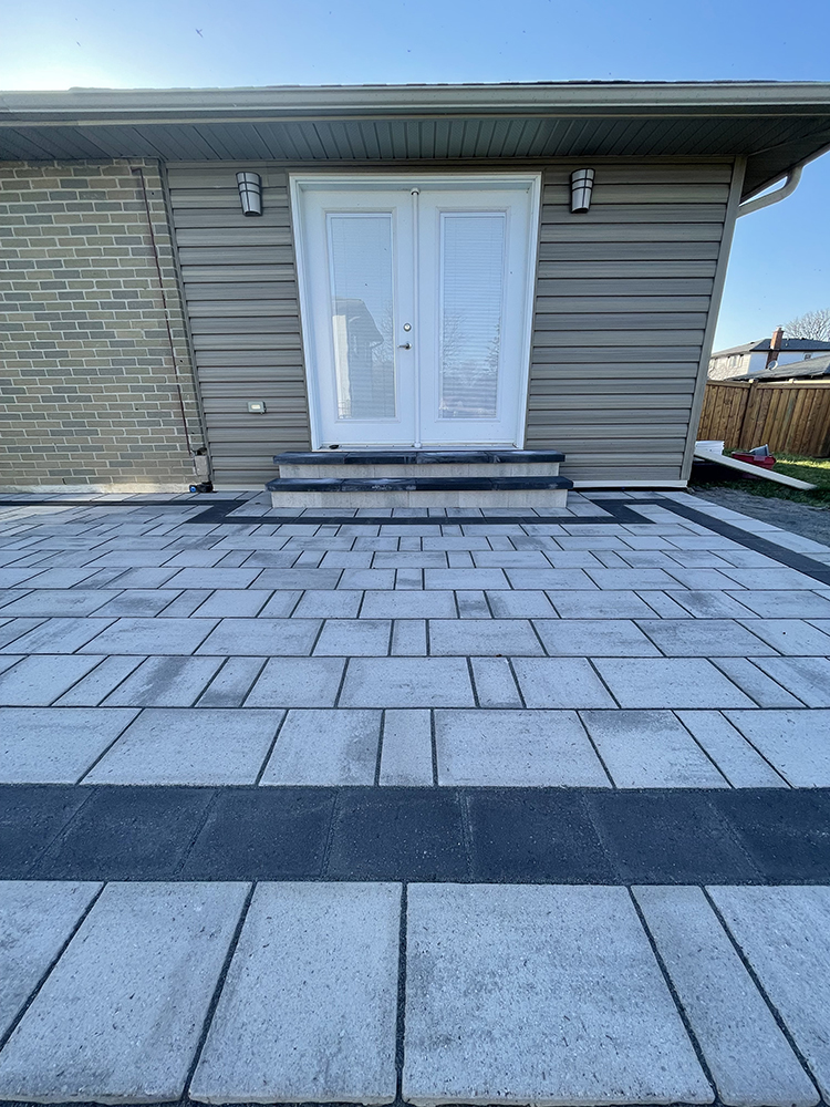 Outdoor patio with light gray and dark gray rectangular stone tiles leading to white double doors on a house.