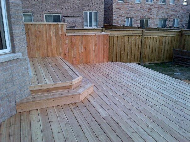 Wooden deck with steps, privacy screen, and fence in a backyard area.