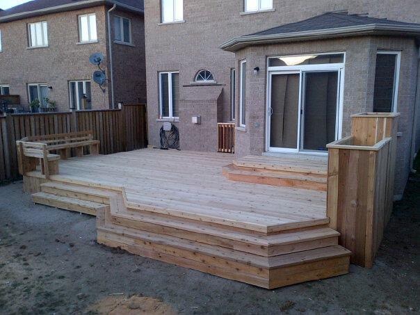 Newly built multi-level wooden deck attached to a brick house with built-in benches and steps.