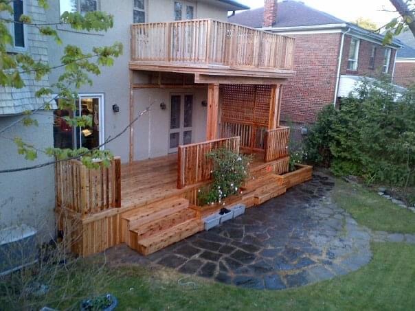 Wooden two-level deck attached to house with steps, railings, and stone patio below.