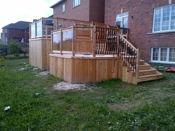 Raised wooden deck attached to a brick house with stairs and black metal railings.