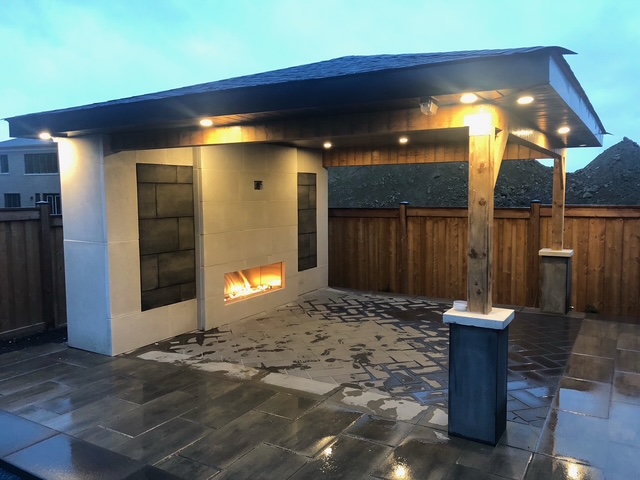Outdoor patio area with lit modern fireplace under a covered pergola at dusk.
