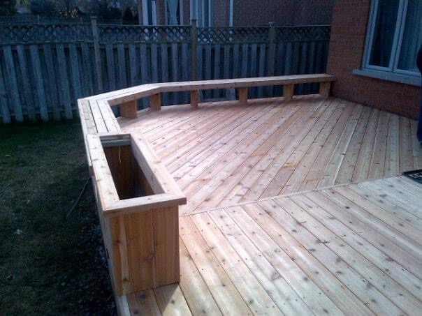 Newly built wooden deck with built-in bench seating and planter box in a fenced backyard.