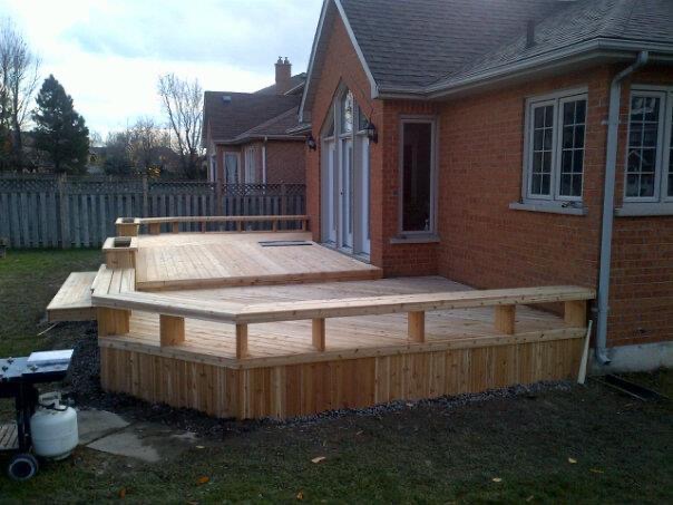 Newly built multi-level wooden deck attached to a brick house in a backyard.