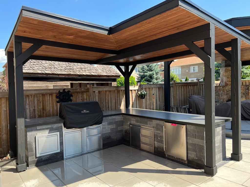 Outdoor kitchen area with a covered patio, stainless steel grill, refrigerator, and storage drawers.