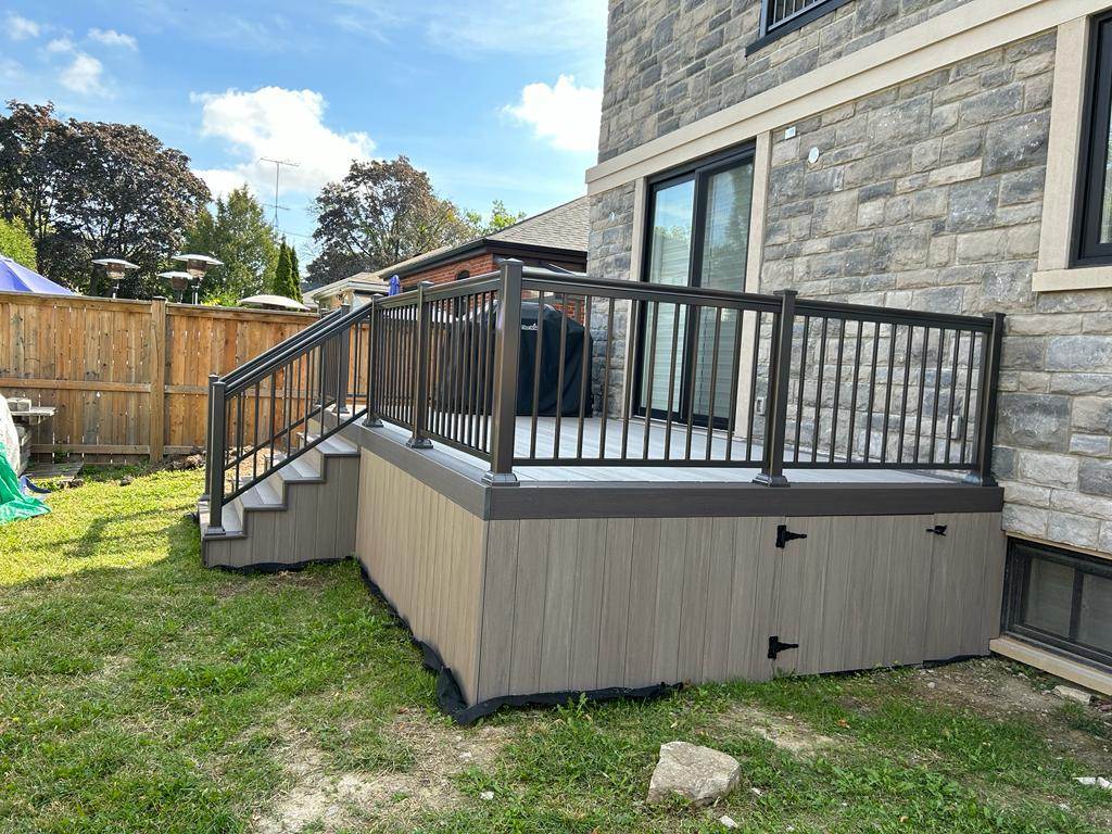 Raised backyard deck with gray railing and stairs attached to stone house exterior.